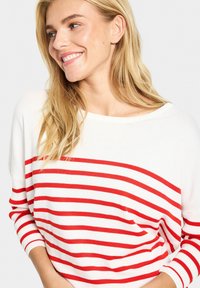 Pull rayé rouge et blanc avec une coupe loose, un col large et des poignets côtelés. Texture douce et design décontracté.