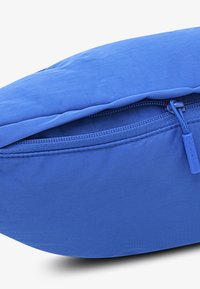 Borsa imbottita blu con una texture di tessuto liscio, chiusura con zip e un tirante sagomato, e forma arrotondata.