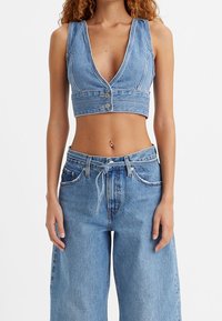 Denimcroppad topp med djup V-ringning, två knappknäppningar och breda axelremmar. Kombinerad med högmidjade, löst sittande blåjeans.