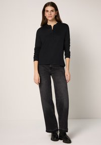 Czarna bluzka z długim rękawem, z falowanym dekoltem i listwą z guzikami, zestawiona z ciemnymi, wysokim stanem, szerokimi dżinsami oraz botkami do kostki.