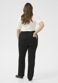 Schwarze gerade Hosen mit hoher Taille, zwei Gesäßtaschen und einer weichen Textur, kombiniert mit einem kurzärmeligen weißen Oberteil.