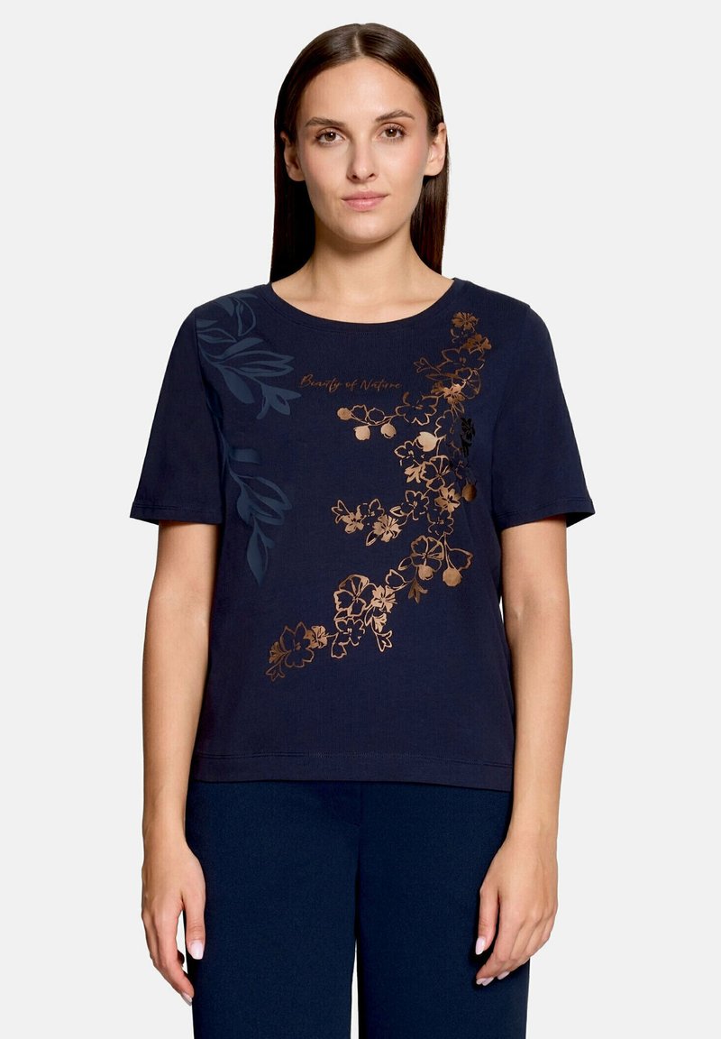 Femme portant un t-shirt bleu marine à manches courtes, décoré d’un motif floral cuivre et bleu foncé sur le devant avec le texte « Beauty of Nature. »