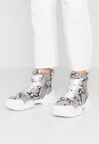 Wysokie sneakersy w szarym i czarnym wzorze węża, z białymi sznurowadłami oraz teksturowaną gumową podeszwą o masywnej sylwetce.