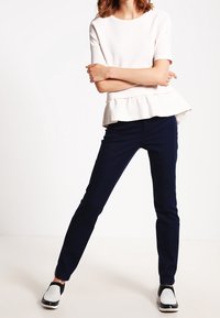 Vit peplumtop med korta ärmar, kombinerad med marinblå slim-fit byxor. Skorna har en svart och vit perforerad design.