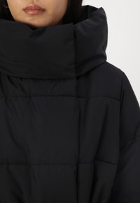 Chaqueta acolchada negra con un cuello alto. Presenta paneles acolchados, textura suave y un corte relajado. Ideal para el clima frío.