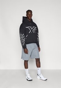 Μαύρη κουκούλα με λευκό γραφικό σχέδιο, γκρι σορτς, άσπρες κάλτσες Nike και άσπρα αθλητικά παπούτσια. Απλή και λειτουργική αθλητική ένδυση.