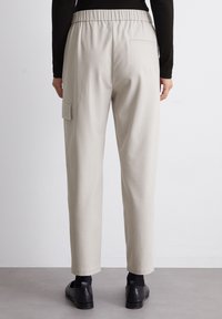 Beige, schmal zulaufende Hose mit einem elastischen Bund und einer Gesäßtasche; verfügt über eine Cargo-Tasche auf der linken Seite. Glatte, weiche Textur.
