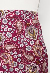 Kuosisati maroon-taustalla, jossa on paisley- ja kukkakuoseja valkoisena, purppurana ja kullanvärisenä. Kevyt kangas, jossa on sileä pinta.