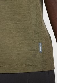 Olive green short-sleeve shirt made of textured fabric, featuring a stitched hem and a small "icebreaker" label on the side.
