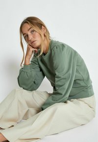 Green sweatshirt featuring puffed sleeves, paired with light-colored wide-leg trousers. Soft fabric and relaxed fit enhance comfort.