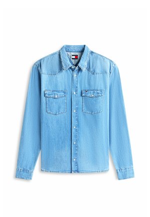 Jasnoniebieska koszula z denimu z długim rękawem, zapinana na guziki, z dwoma kieszeniami na piersi z patkami oraz małą naszywką z logo w kolorach czerwonym, białym i granatowym na prawej kieszeni.