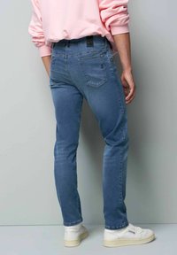 Blauwe denim jeans met een slim fit, voorzien van een donkere taillebandlabel, twee achterzakken en subtiele wassing op de dijen. Gecombineerd met witte sneakers.