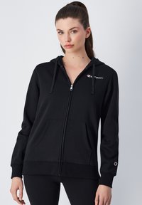Felpa nera con zip realizzata in morbido misto cotone, dotata di tasca frontale, cappuccio con cordino e logo ricamato sul petto e sulla manica.