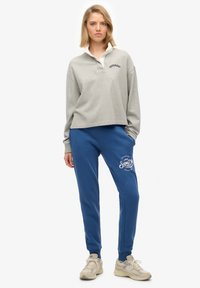 Szara krótka koszulka polo z długim rękawem i białym kołnierzykiem, zestawiona z niebieskimi dresami z logo. Uzupełniona beżowymi sneakerami.