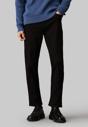 Czarne spodnie o prostym kroju w komplecie z teksturowanym niebieskim swetrem z dzianiny oraz czarnymi skórzanymi butami. Skupienie na eleganckim, minimalistycznym wzornictwie.