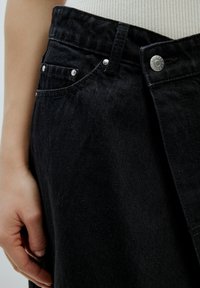 Schwarze Denim-Hosen mit einem klassischen Design, seitlichen Taschen, einem Knopfverschluss und sichtbaren Nähten. Glatte Textur.