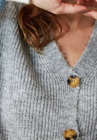 Graue Strickjacke mit V-Ausschnitt, ausgestattet mit drei großen goldenen Knöpfen. Die Textur ist weich und gerippt und vermittelt ein gemütliches Aussehen.