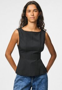 T-shirt sans manches noir avec un décolleté carré, forme structurée et coutures verticales ; associé à un jean en denim bleu.