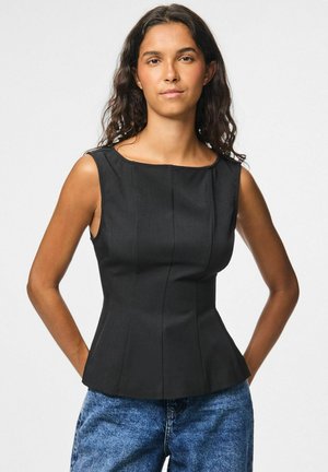 Top nero senza maniche con scollatura squadrata, forma strutturata e cuciture verticali; abbinato a jeans in denim blu.