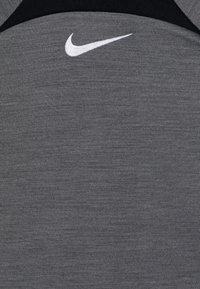 Šedé sportovní tričko s texturovanou látkou, s bílým logem Nike na hrudi a černými akcenty v okolí výstřihu.