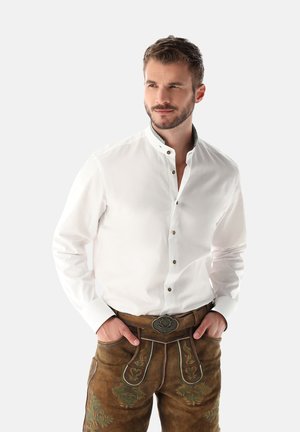 Weißes Langarmhemd mit Stehkragen und braunen Knopfakzenten, kombiniert mit braunen Lederhosen, die mit grüner Blumenstickerei verziert sind.