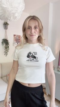 Bijela skraćena majica s tiskom ilustracije psa i tekstom "Imao si težak dan? Tu sam za tebe!" u crnoj boji. Mekana tkanina, ležeran kroj.