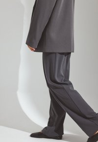 Harmaa räätälöity bleiseri, joka on yhdistetty samansävyisiin leveälahkeisiin housuihin, valmistettu sileästä kankaasta, jossa on puhtaat linjat ja hienovaraiset varjoefektit.