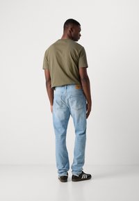 Olive green cotton T-shirt, light blue denim jeans with a straight fit, and black sneakers with white stripes, viewed from the back.
