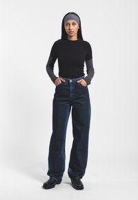 Jeans de mezclilla oscura de tiro alto con corte recto, combinados con una camiseta negra ajustada y una capa inferior de manga larga gris; zapatos negros sencillos.