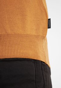 Senfgelber gestrickter Pullover mit geripptem Saum und Seitendetail. Verfügt über ein kleines schwarzes Etikett mit der Aufschrift "CLIPPER" an der Seite.