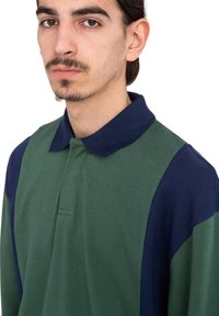 Polo tričko s zelenými a námorníckymi pruhmi, s klasickým golierom a textúrovanou látkou. Obsahuje golier na tri gombíky a bežný strih.