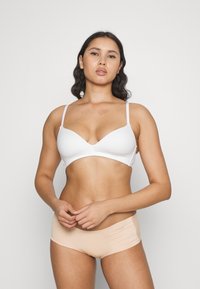 Witte draadloze bh met een V-vormige halslijn en dunne bandjes, gecombineerd met naadloze naturel slipjes met een subtiele ruching aan de zijkanten.