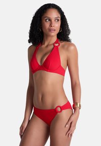 Ensemble de bikini rouge comprenant un haut triangulaire avec des accents en anneau et un système de fermeture à nouer, accompagné d'un bas assorti également orné d'anneaux. Texture lisse.