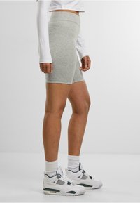 Pantaloni ciclisti grigi a vita alta realizzati in un tessuto morbido e elastico, abbinati a sneakers sportive bianche e calze bianche a costine.