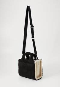 Petit sac à main rectangulaire noir et crème en peluche, avec des poignées courtes et une longue bandoulière noire réglable.