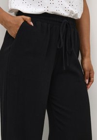 Zwarte wijde broek met een gestructureerde stof, elastische tailleband en verstelbaar trekkoord. Beschikt over zijzakken voor extra gemak.
