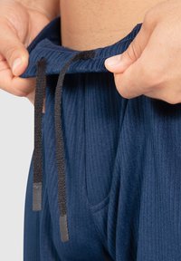 Marineblauwe geribde broek met een tailleband met trekkoord. De trekkoorden zijn zwart met plastic punten. Inclusief zijzakken en een textuurstof.
