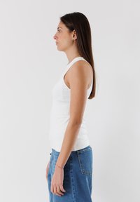 Top in cotone bianco con un design aderente, spalline larghe e una texture liscia, abbinato a jeans di denim blu a vita alta.