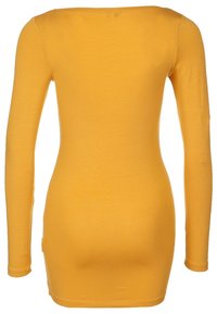 Dopasowana sukienka z długim rękawem, wykonana z żółtej bawełny, z okrągłym dekoltem i gładką teksturą, bez widocznych zapięć ani wzorów.