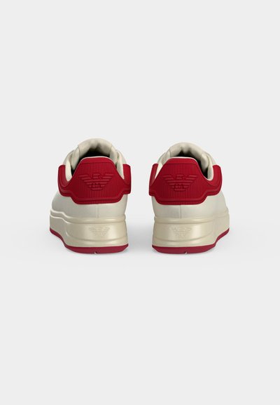Ζευγάρι κρεμ και κόκκινων sneakers χαμηλού πάτου, εμφανιζόμενα από πίσω με ανάγλυφο λογότυπο στη φτέρνα και κόκκινες λεπτομέρειες στο γιακά και στη σόλα.