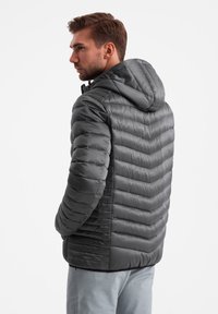 Grijze geïsoleerde jas met een capuchon, gekenmerkt door een chevron-quiltpatroon, een gladde textuur en een ritssluiting.