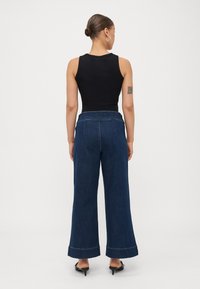 Top negro sin mangas combinado con pantalones de denim de pierna ancha de color azul oscuro que presentan costuras en contraste y una cintura alta. Textura suave en todo el conjunto.