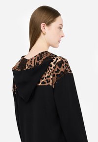 Felpa nera con cappuccio caratterizzata da un motivo leopardato sul cappuccio e sulle spalle, con un corpo nero a contrasto, texture liscia e cappuccio regolabile con coulisse.