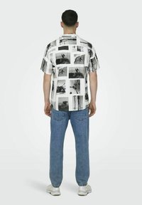 Camicia a maniche corte nera e bianca con stampa fotografica. Abbinata a jeans azzurri chiari e sneakers bianche, vista da dietro.