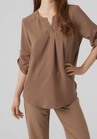 Blusa marrone leggera con apertura a metà bottone e maniche a ¾, abbinata a pantaloni coordinati, caratterizzati da una texture liscia.