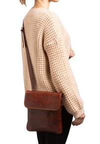 Borsa a spalla in pelle marrone con una texture liscia e un flap arrotondato. Presenta una lunga tracolla regolabile e dettagli di cucitura sottili.