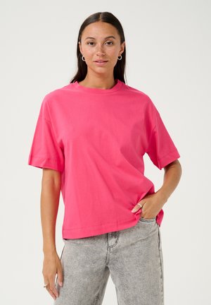 T-shirt en coton rose à manches courtes et col rond, présentant une coupe décontractée et une texture lisse. Associé à un jean gris clair.