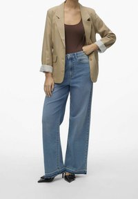 Beige blazer with rolled cuffs over a brown bodysuit, paired with high-waisted, wide-leg blue jeans and pointed black heels.