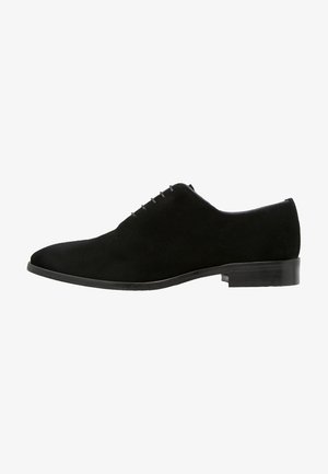 Scarpa Oxford da uomo in suede nero con chiusura a lacci chiusi, tacco basso impilato e punta arrotondata, mostrata di profilo.