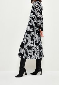 Vestido negro con estampado floral y diseño de paisley blanco, de mangas largas y falda plisada. Combinado con botas altas de tacón negro.